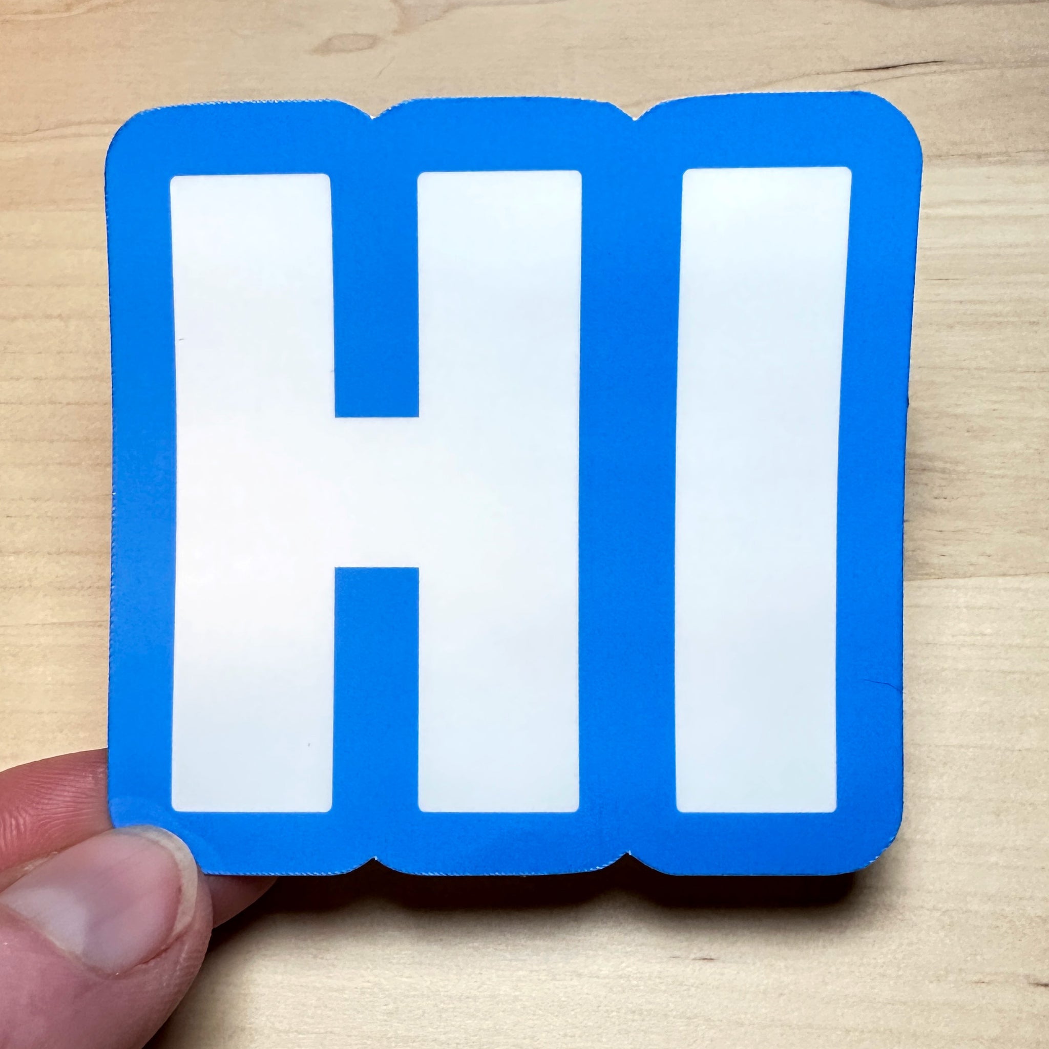 photo of square vinyl sticker with the word HI in white with a blue background