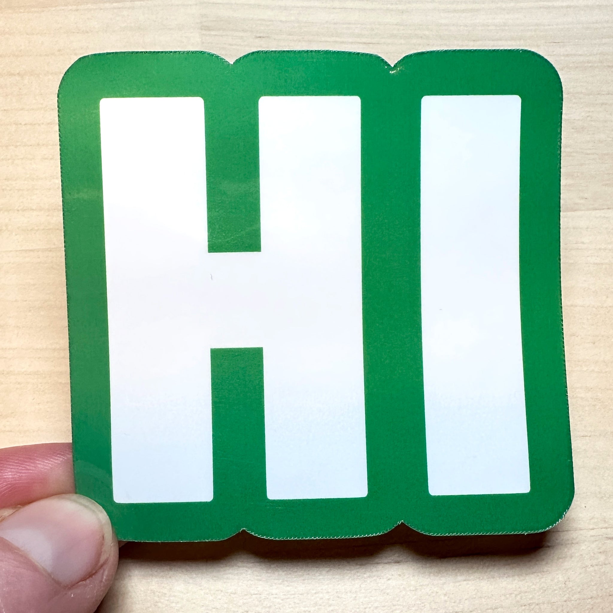 photo of square vinyl sticker with the word HI in white with a green background
