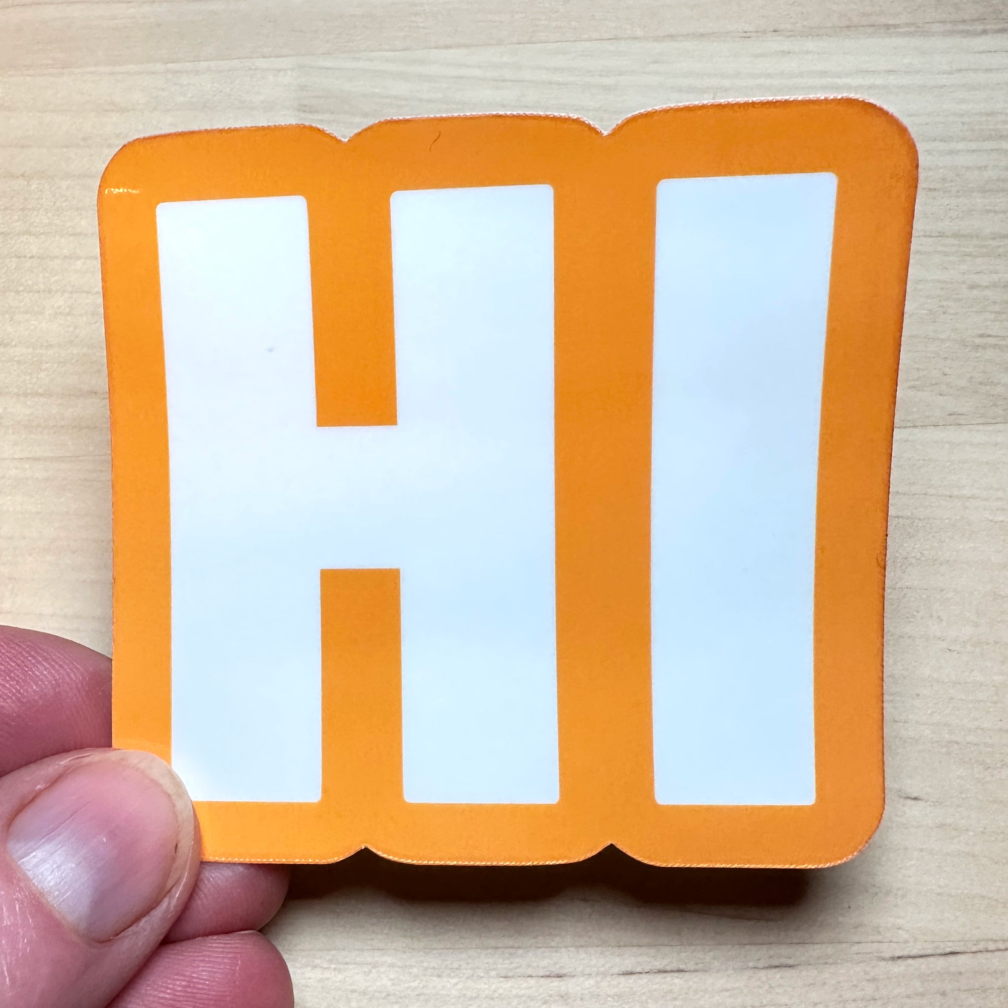 photo of square vinyl sticker with the word HI in white with an orange background