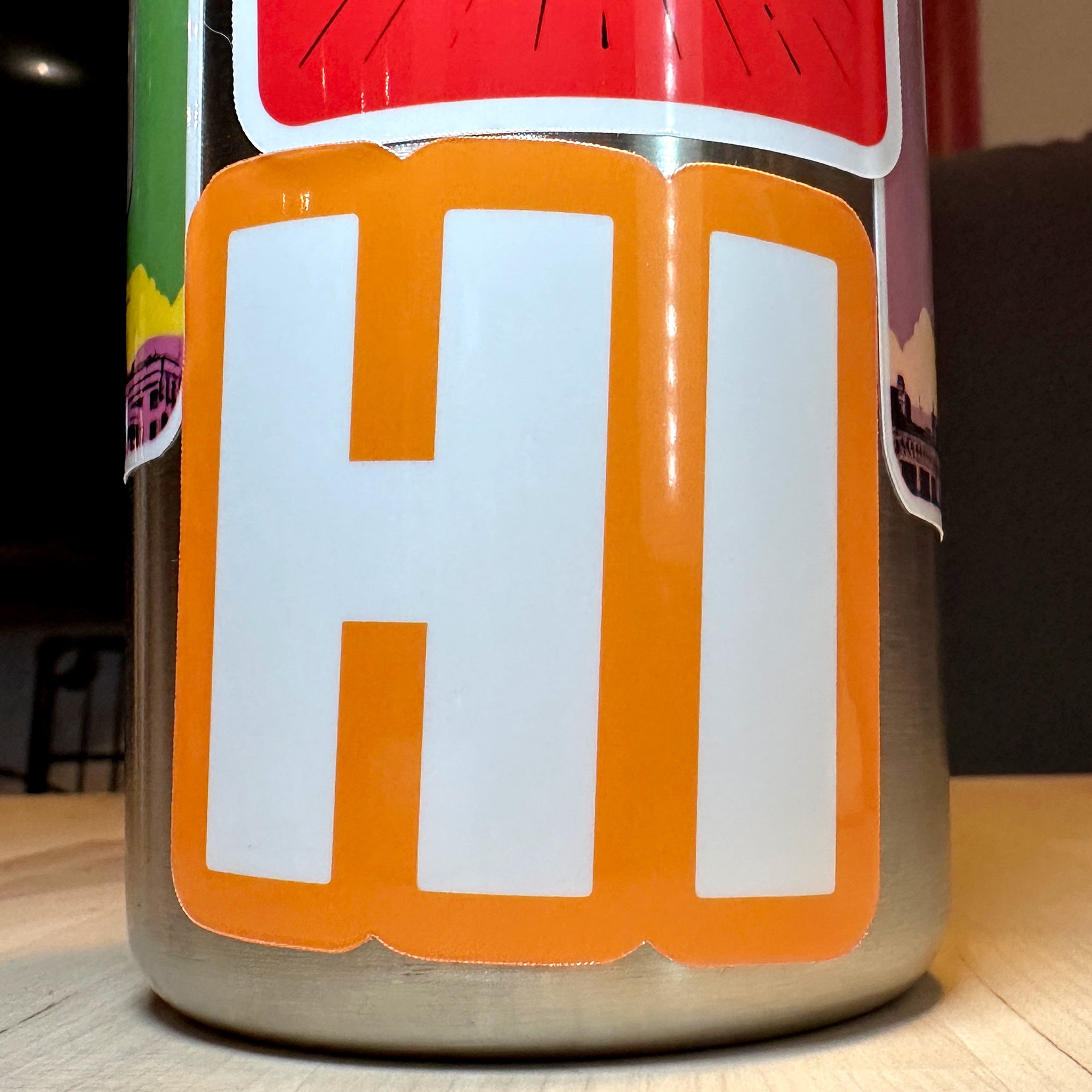 photo of square vinyl sticker with the word HI in white with an orange background on a metal water bottle