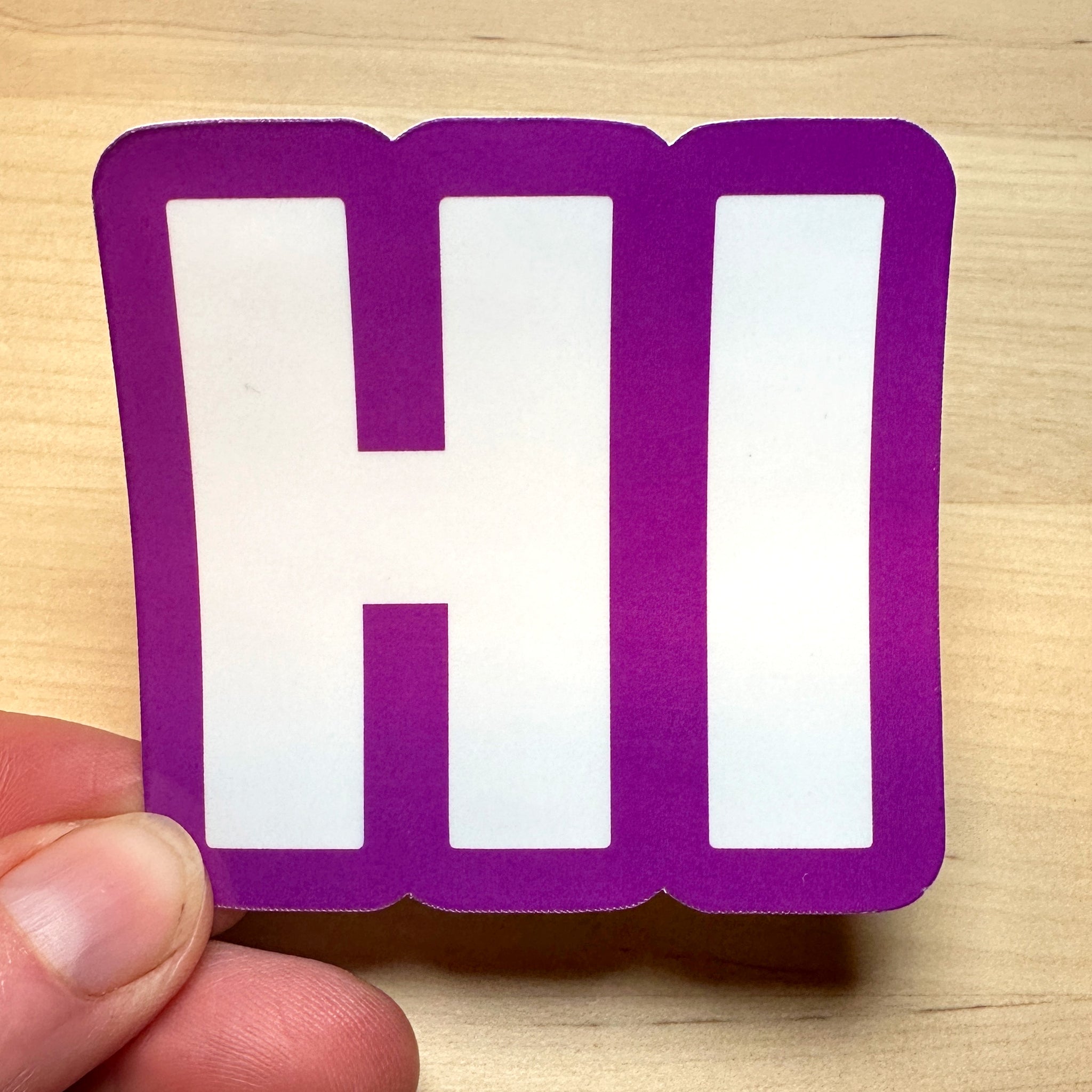 photo of square vinyl sticker with the word HI in white with a purple background