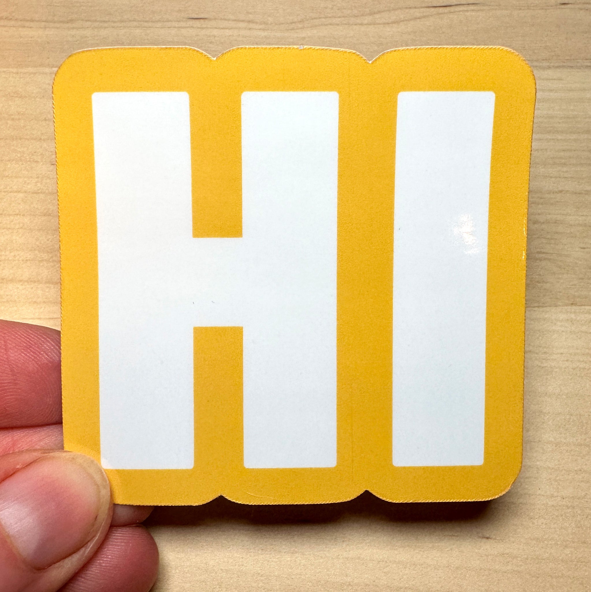 photo of square vinyl sticker with the word HI in white with a yellow background