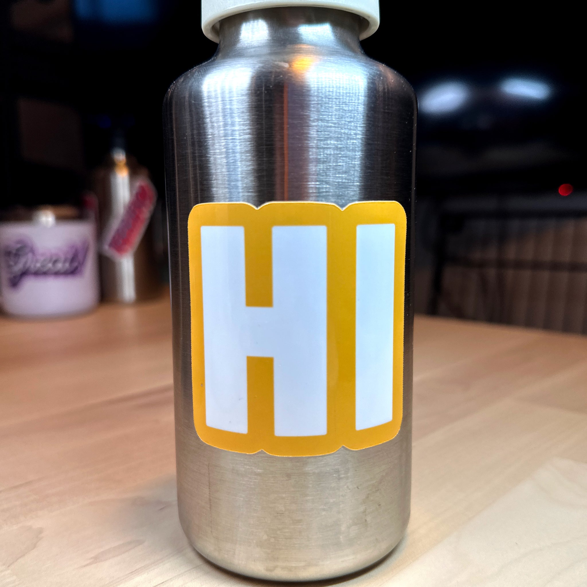 photo of square vinyl sticker with the word HI in white with a yellow background on a metal water bottle