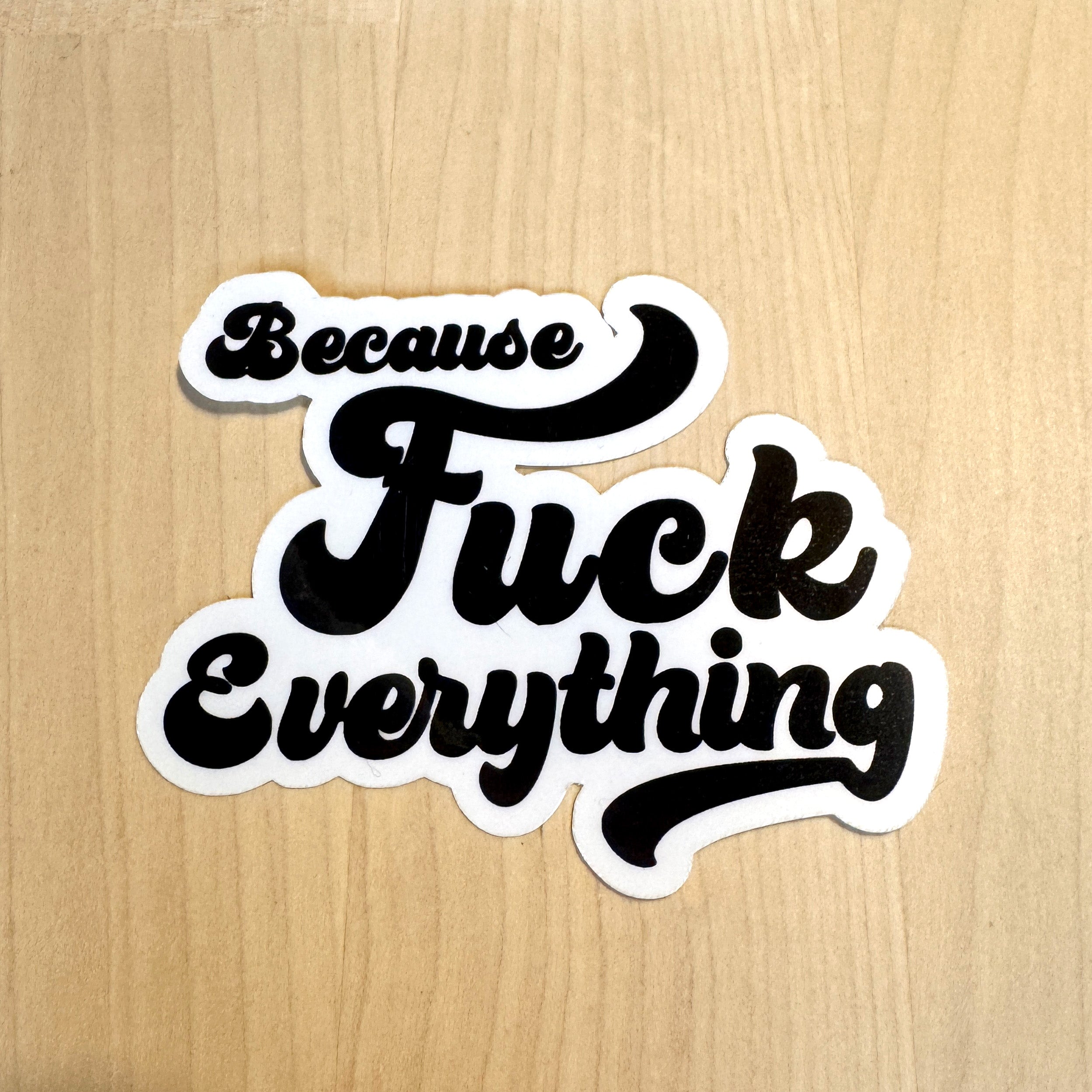 White vinyl sticker with the phrase because fuck everything in cursive lettering, on a wood background