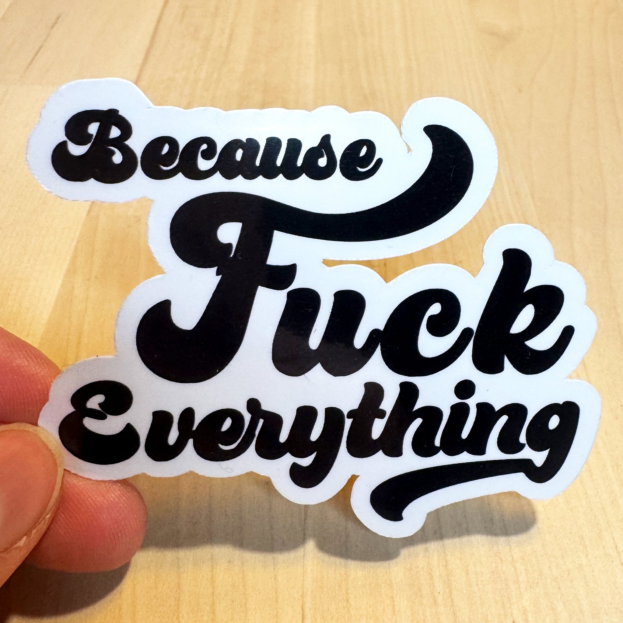 White vinyl sticker with the phrase because fuck everything in cursive lettering, on a wood background