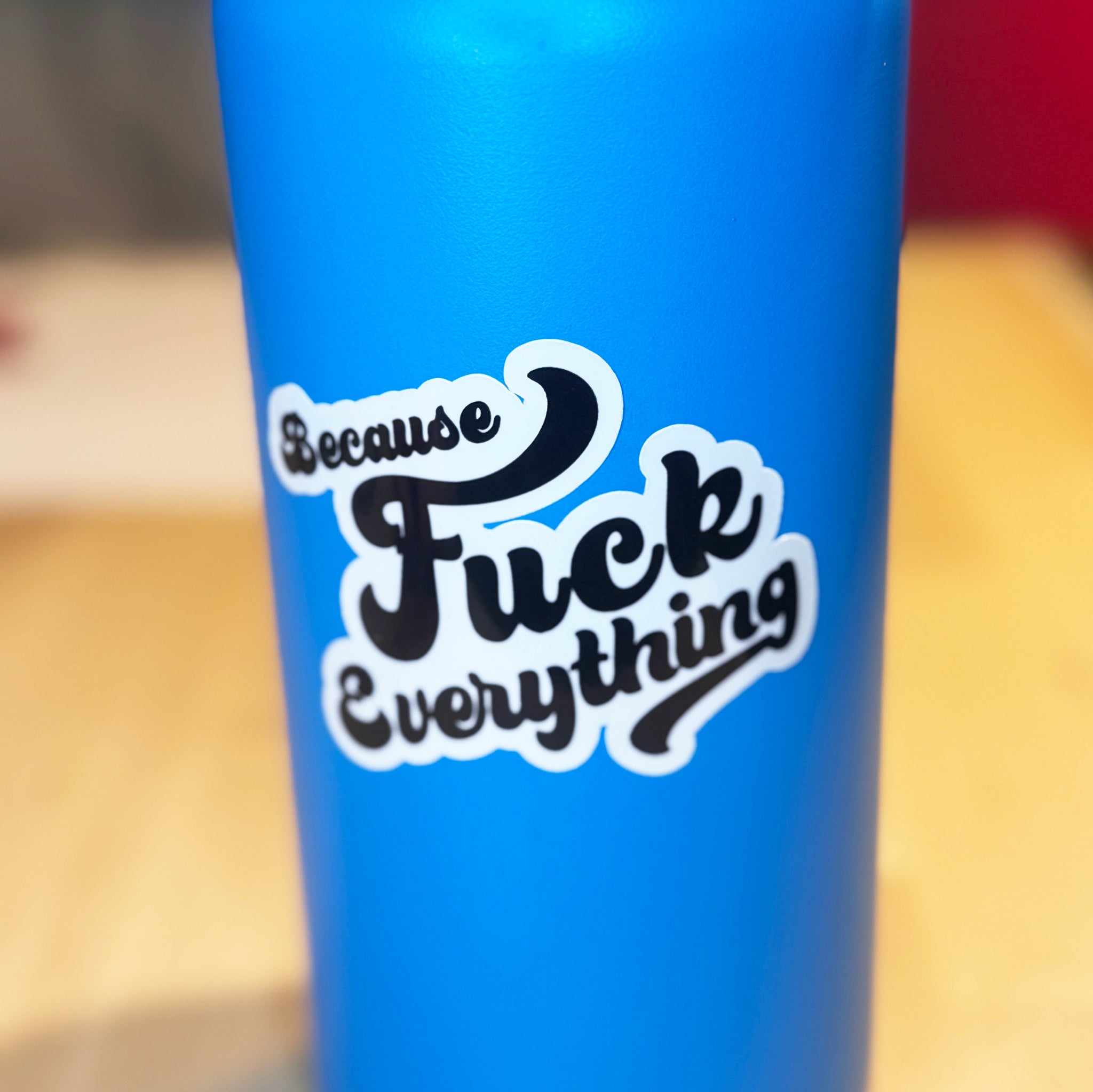 White vinyl sticker with the phrase because fuck everything in cursive lettering, on a blue water bottle