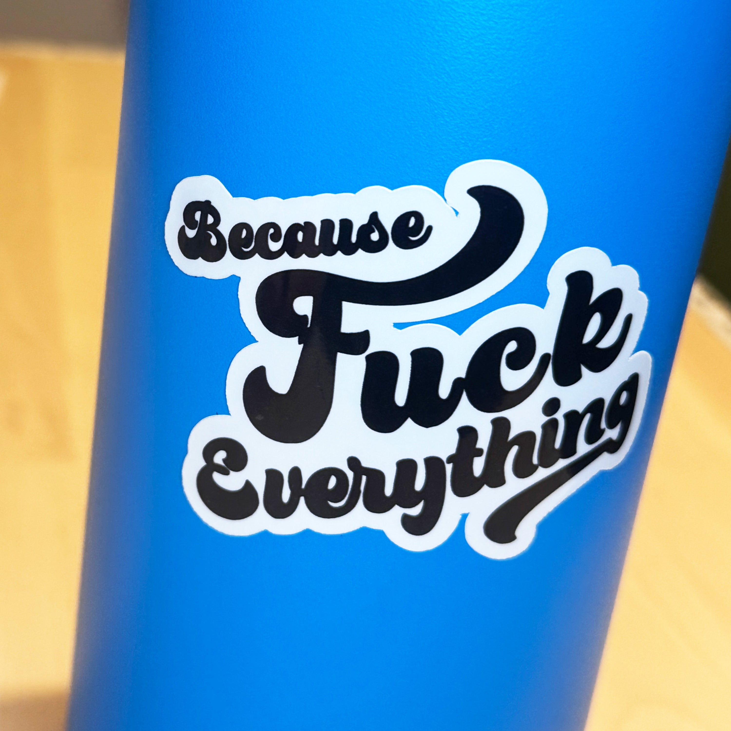 White vinyl sticker with the phrase because fuck everything in cursive lettering, on a blue water bottle