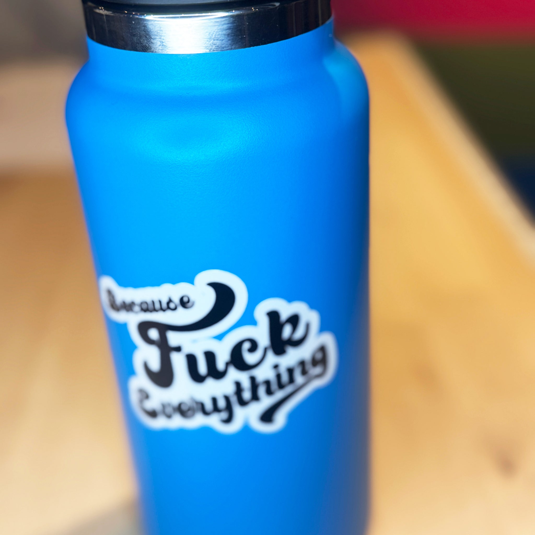 White vinyl sticker with the phrase because fuck everything in cursive lettering, on a blue water bottle