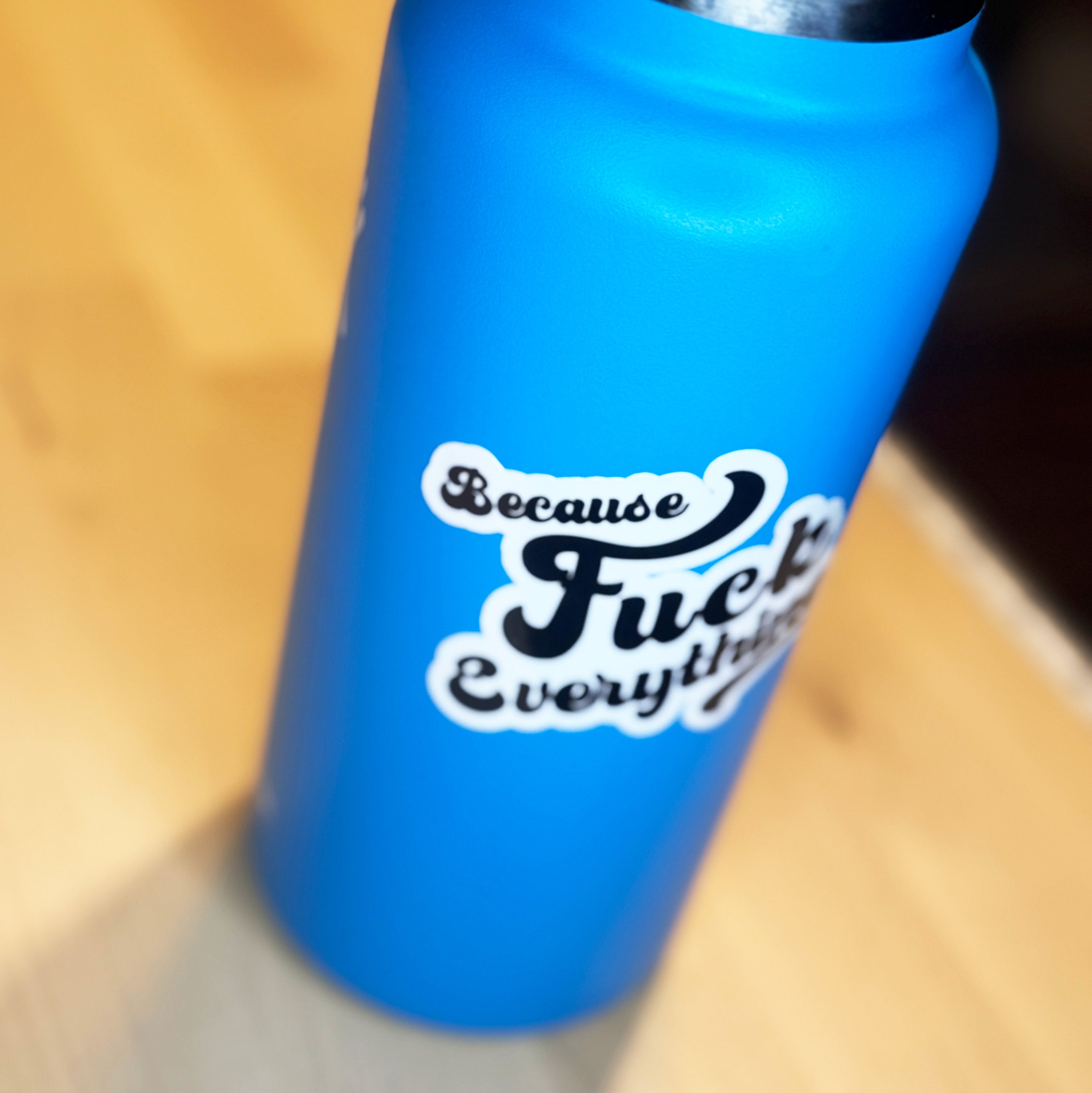White vinyl sticker with the phrase because fuck everything in cursive lettering, on a blue water bottle