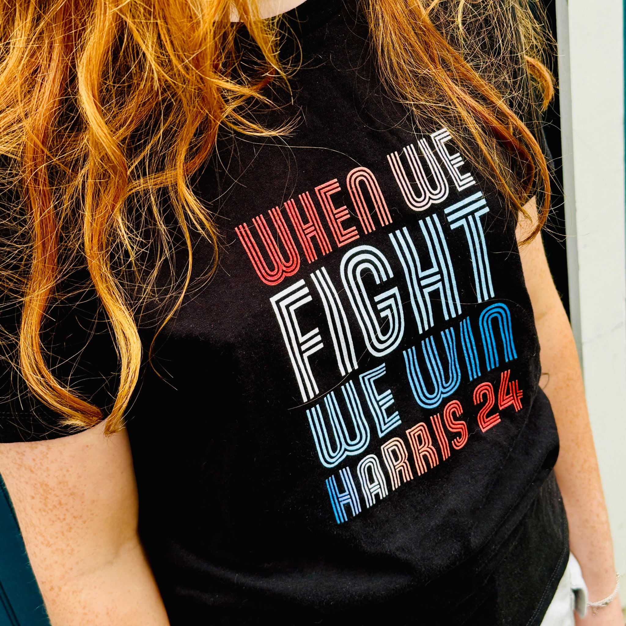 woman with red hair wearing black women shirt with when we fight we win harris 24 in red white and blue blended text