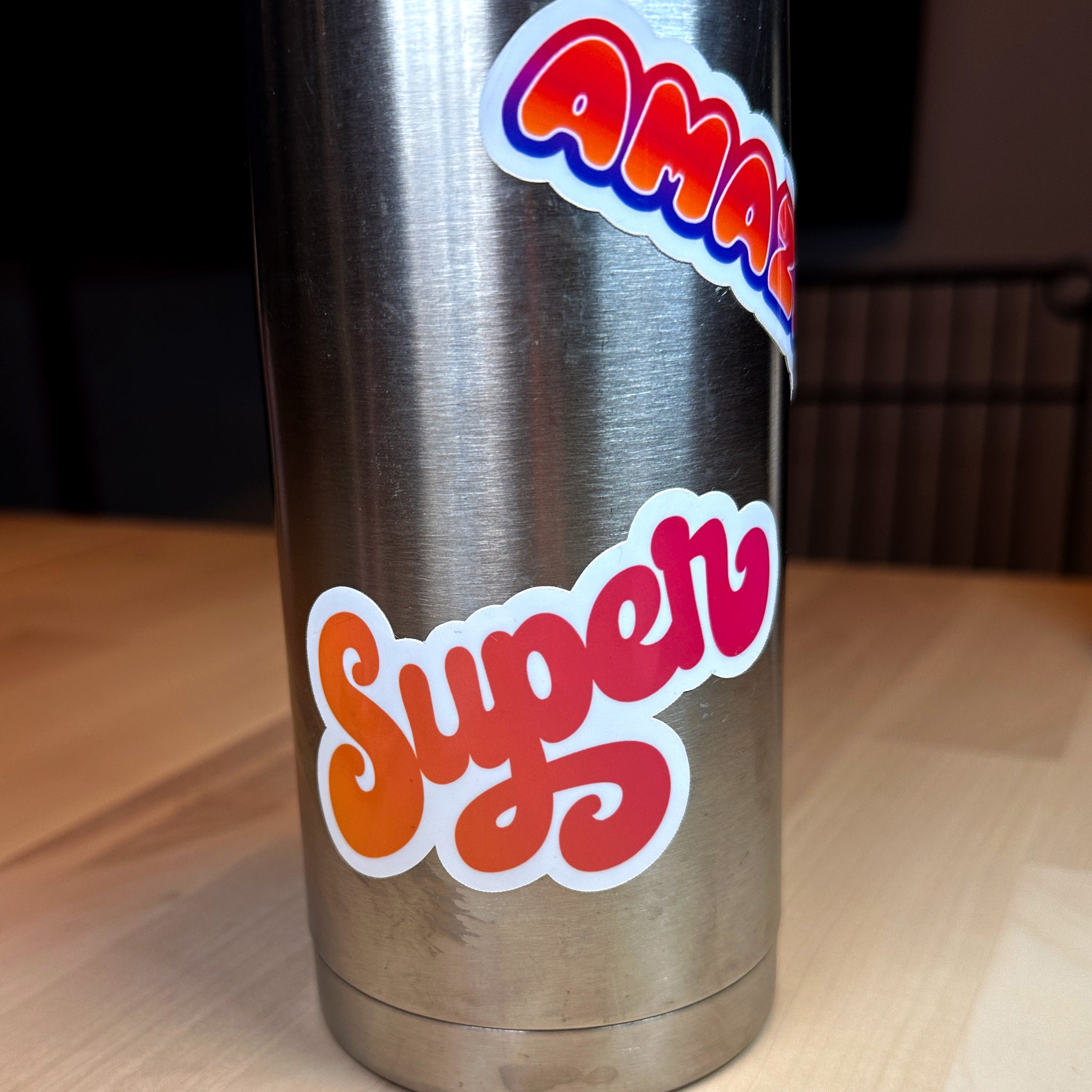 photo of a metal water bottle with waterproof vinyl sticker with the word SUPER in an orange to red blend of color and amazing with a blend