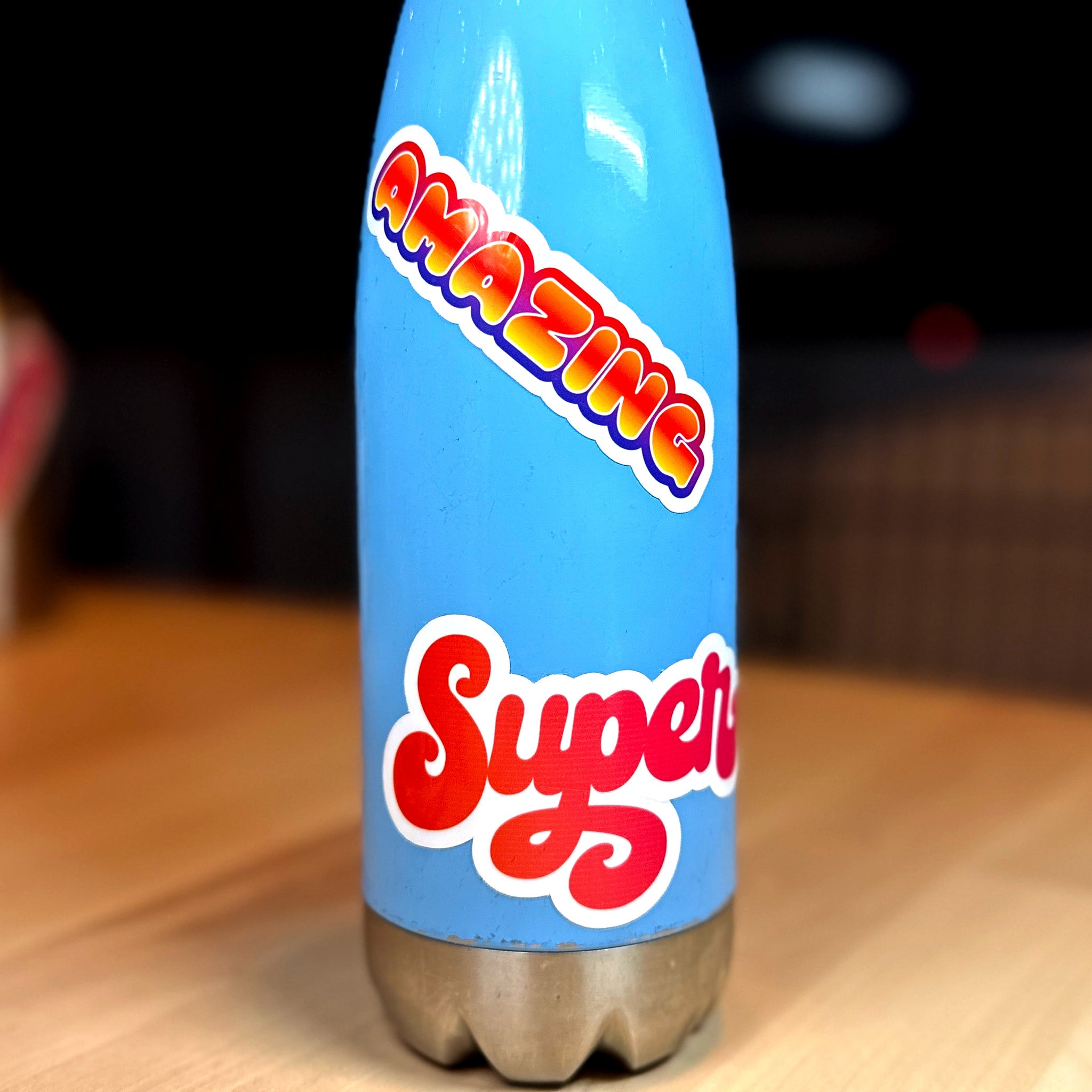 photo of a blue water bottle with waterproof vinyl sticker with the word SUPER in an orange to red blend of color and amazing with a blend