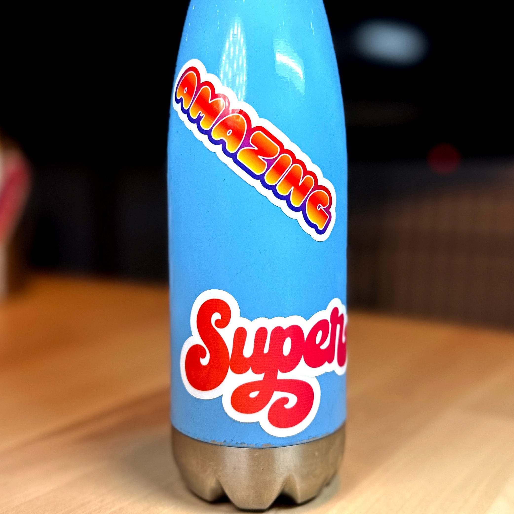 photo of vinyl sticker with the word amazing in orange blend with red and purple blend outline on a blue metal water bottle