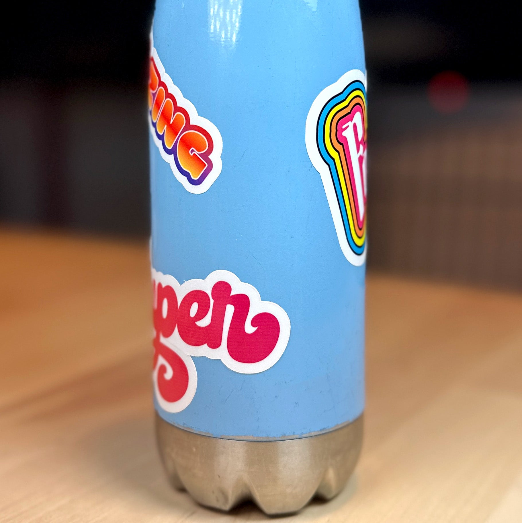 photo of a blue water bottle with partial views of waterproof vinyl sticker with the word SUPER in an orange to red blend of color and amazing with a blend