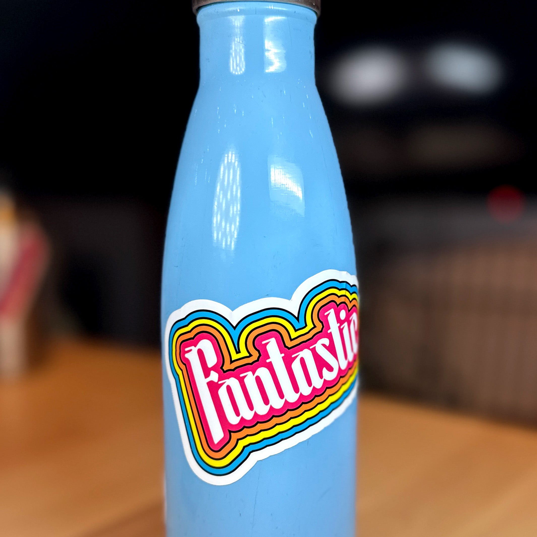 photo of a waterproof sticker on a blue metal water bottle that features the word "Fantastic!" with outlines of pink, orange, yellow and blue