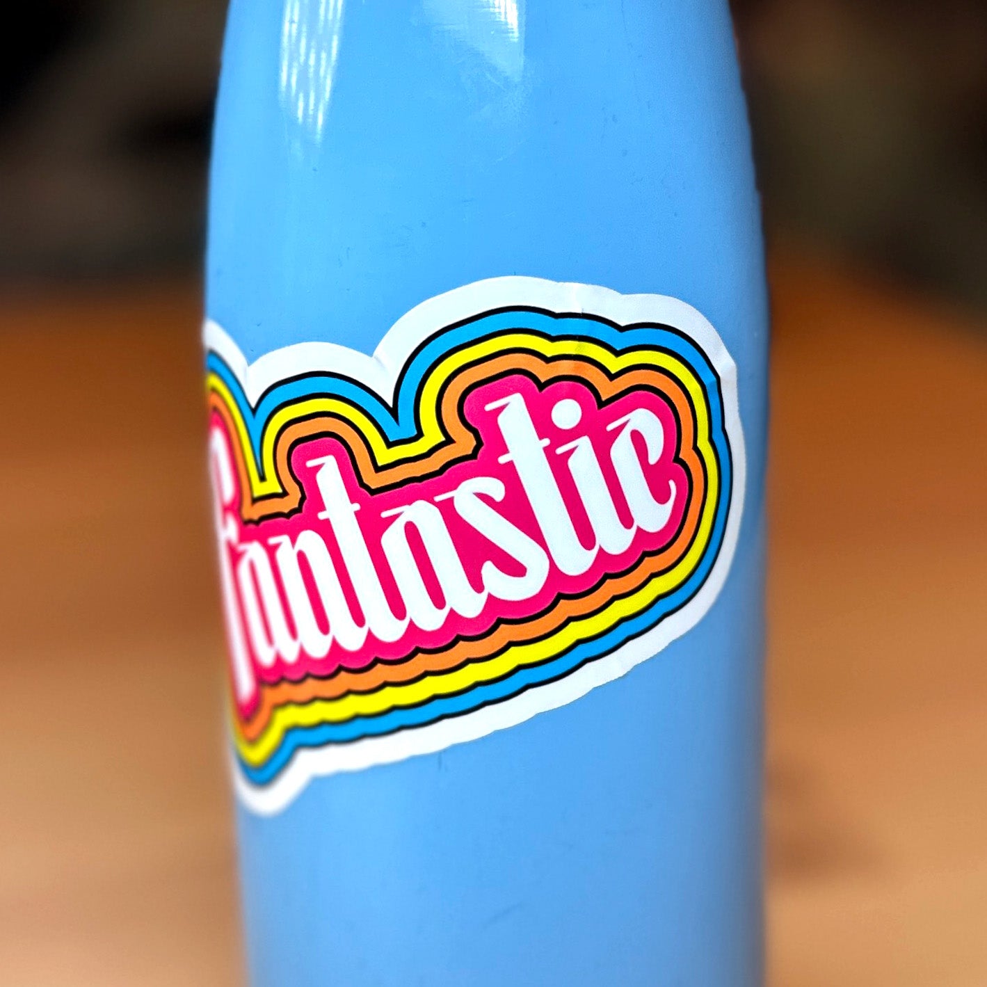 close up photo of a waterproof sticker on a blue metal water bottle that features the word "Fantastic!" with outlines of pink, orange, yellow and blue