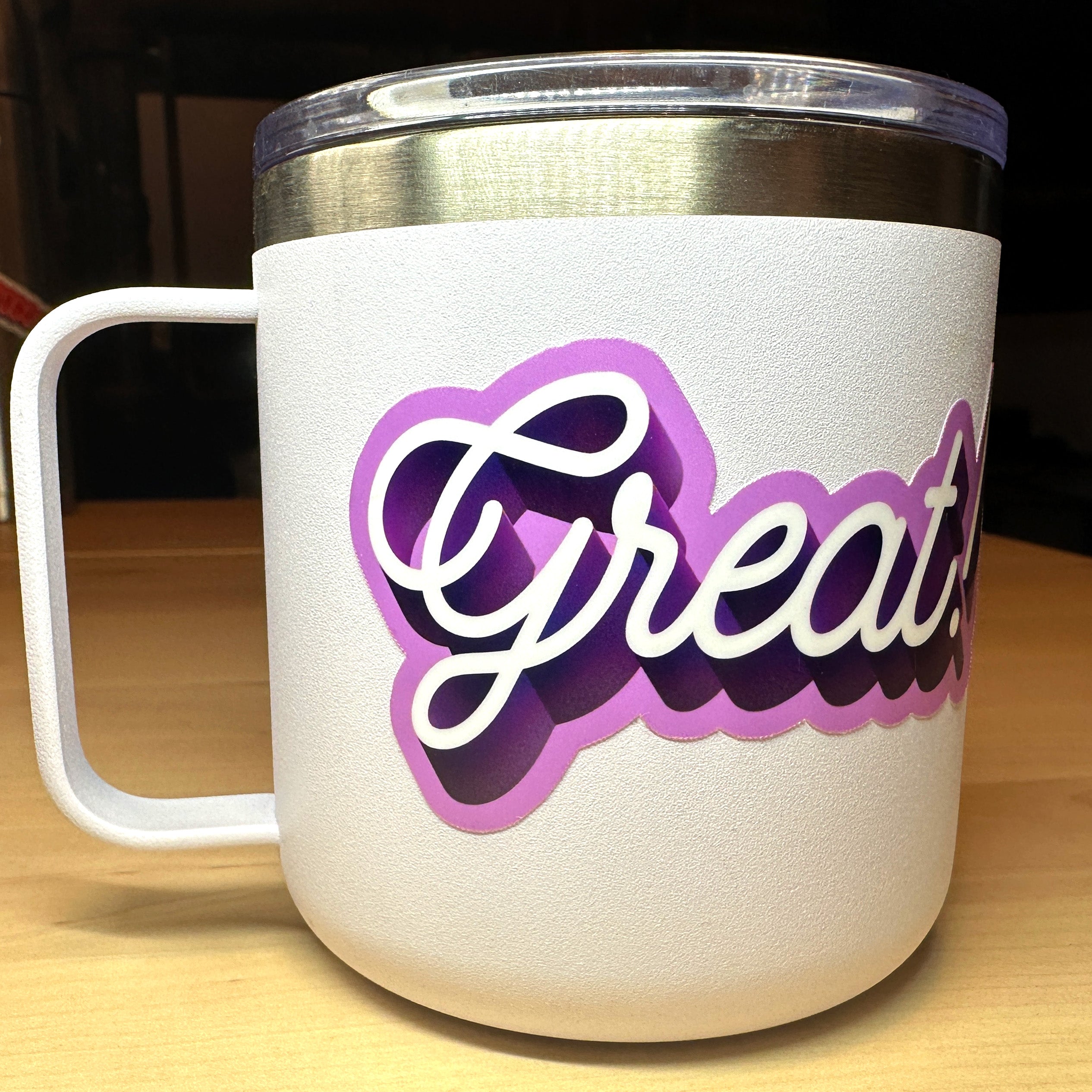 photo of a waterproof vinyl sticker with the word Great in white cursive with dark and light purple outline on a white mug