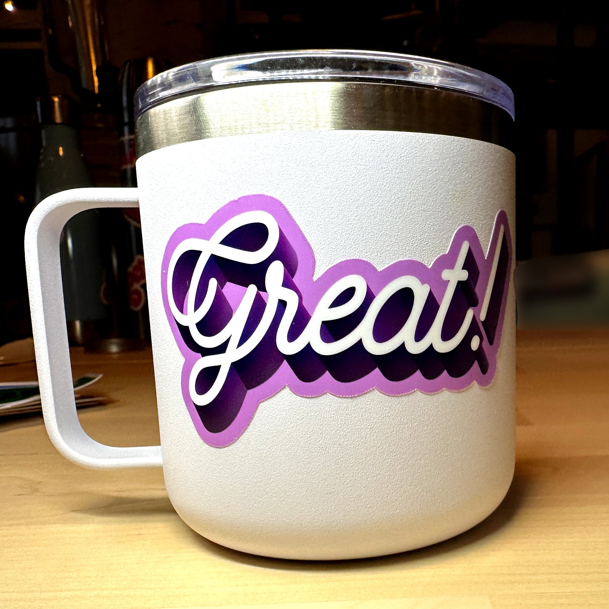 photo of a waterproof vinyl sticker with the word Great in white cursive with dark and light purple outline on a white mug