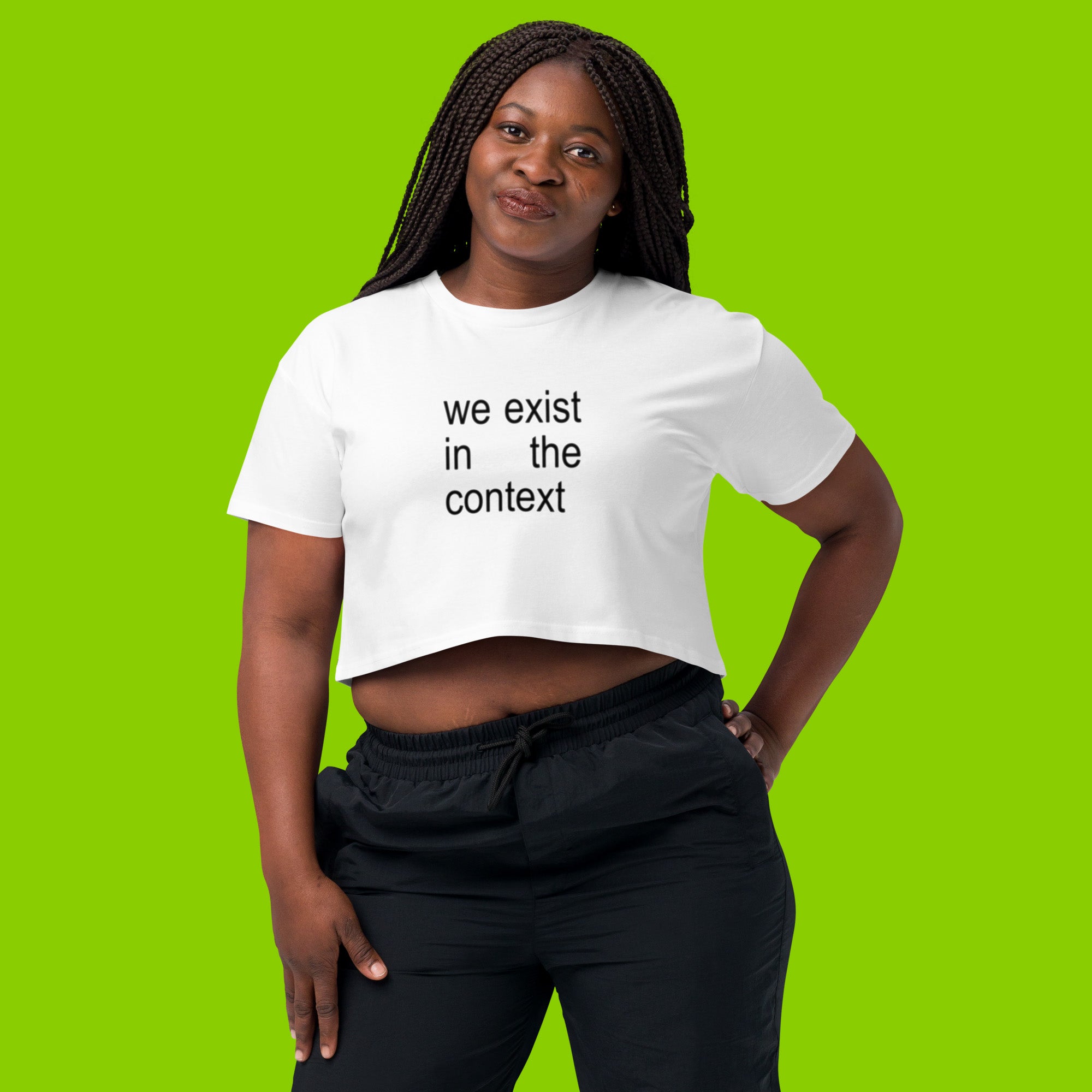 woman wearing white women's crop top t-shirt with the phrase we exist in the context from kamala harris and charli xcx brat