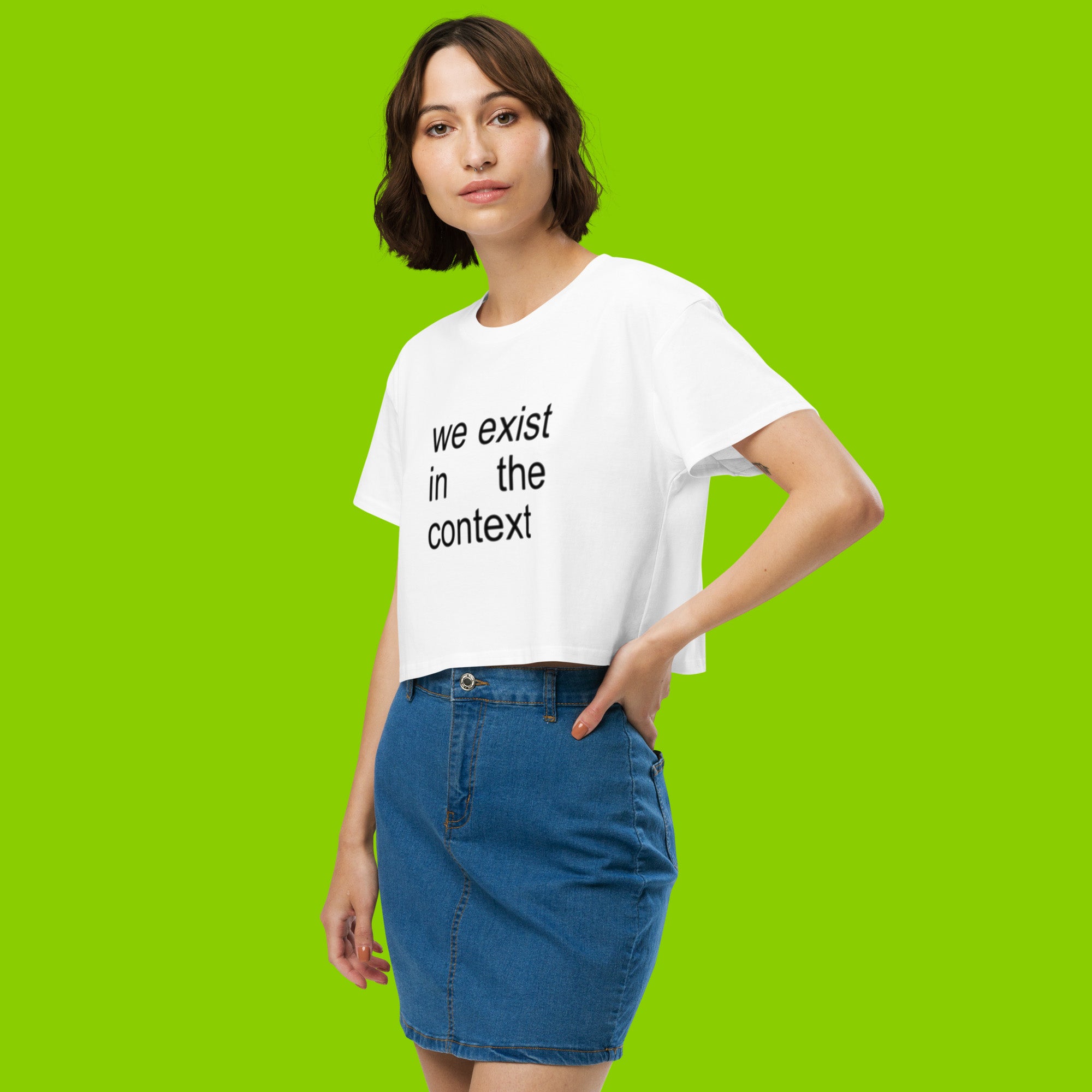 woman wearing white women's crop top t-shirt with the phrase we exist in the context from kamala harris and charli xcx brat