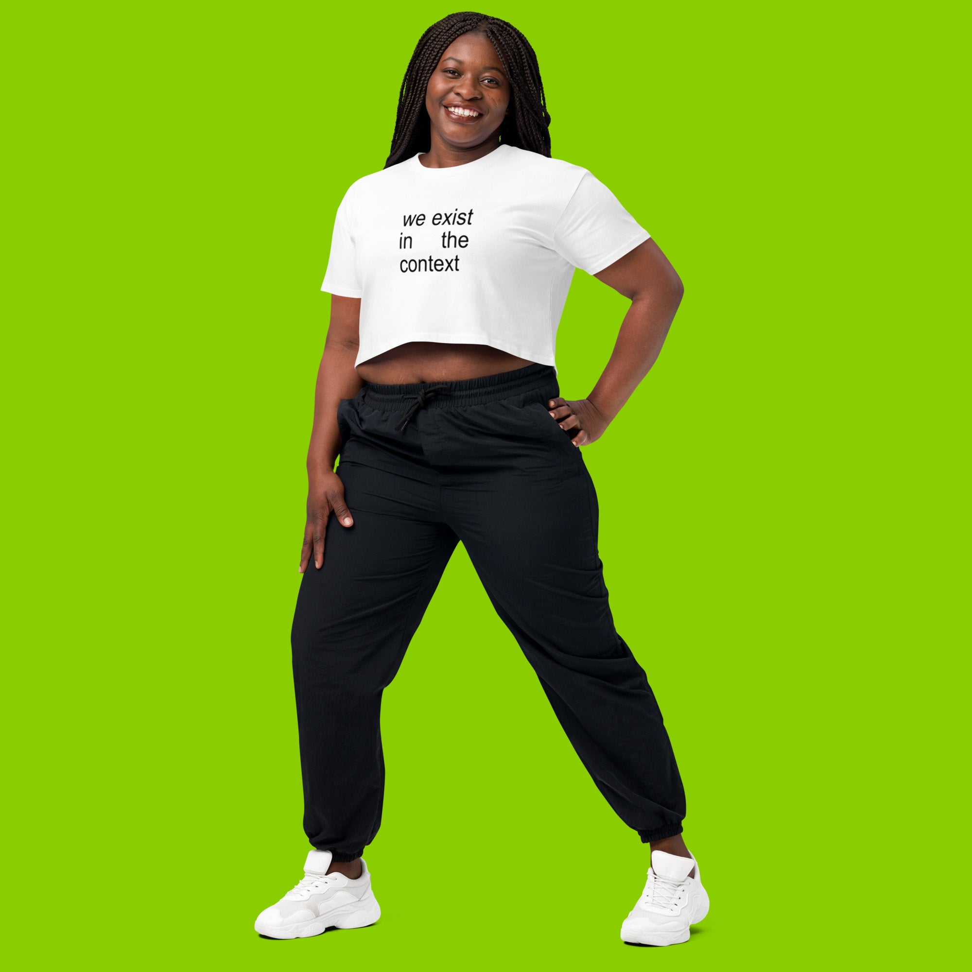 woman wearing white women's crop top t-shirt with the phrase we exist in the context from kamala harris and charli xcx brat