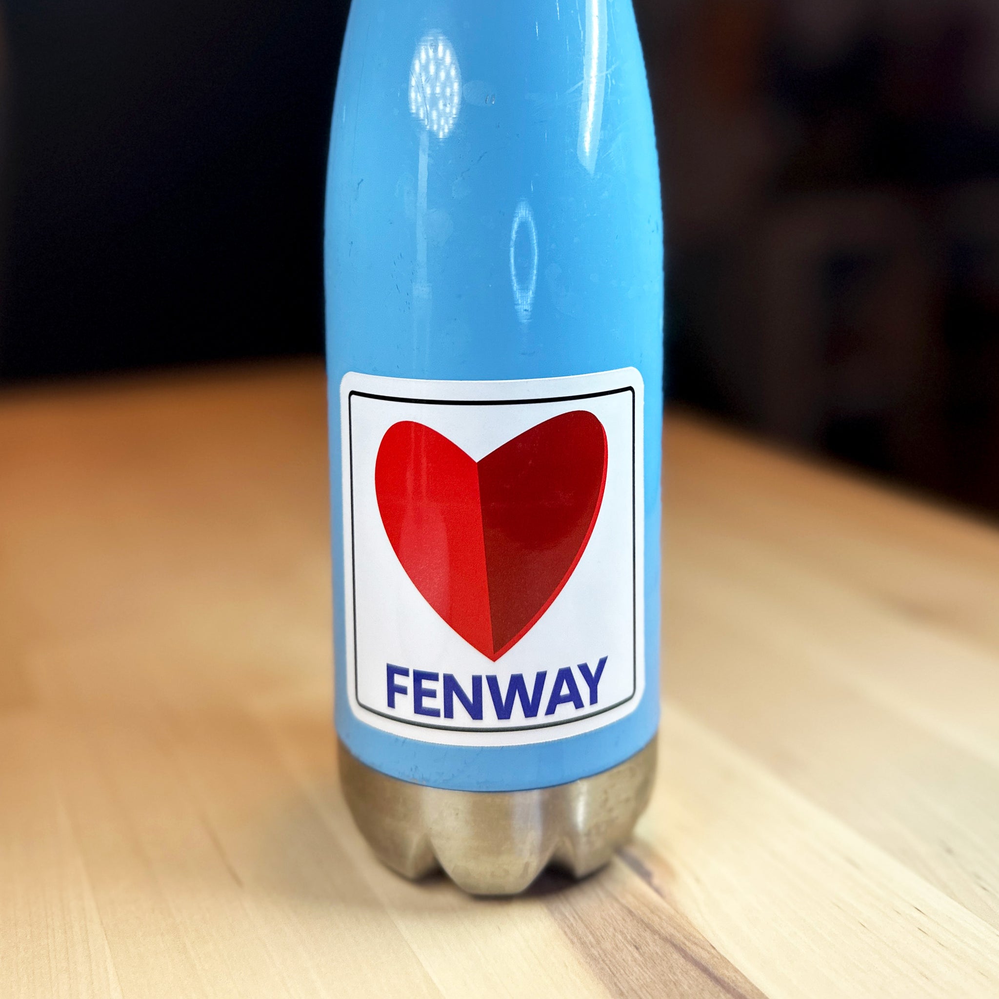 photo of a square vinyl sticker with the word FENWAY and a heart in the style of the boston citgo sign on a blue metal bottle