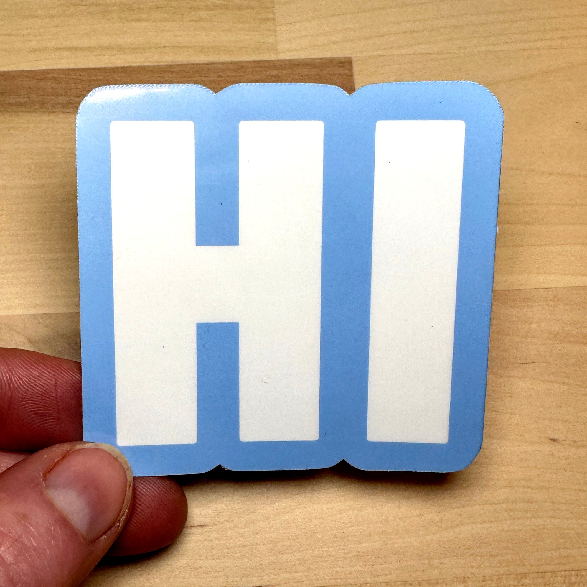 photo of square vinyl sticker with the word HI in white with a light blue background