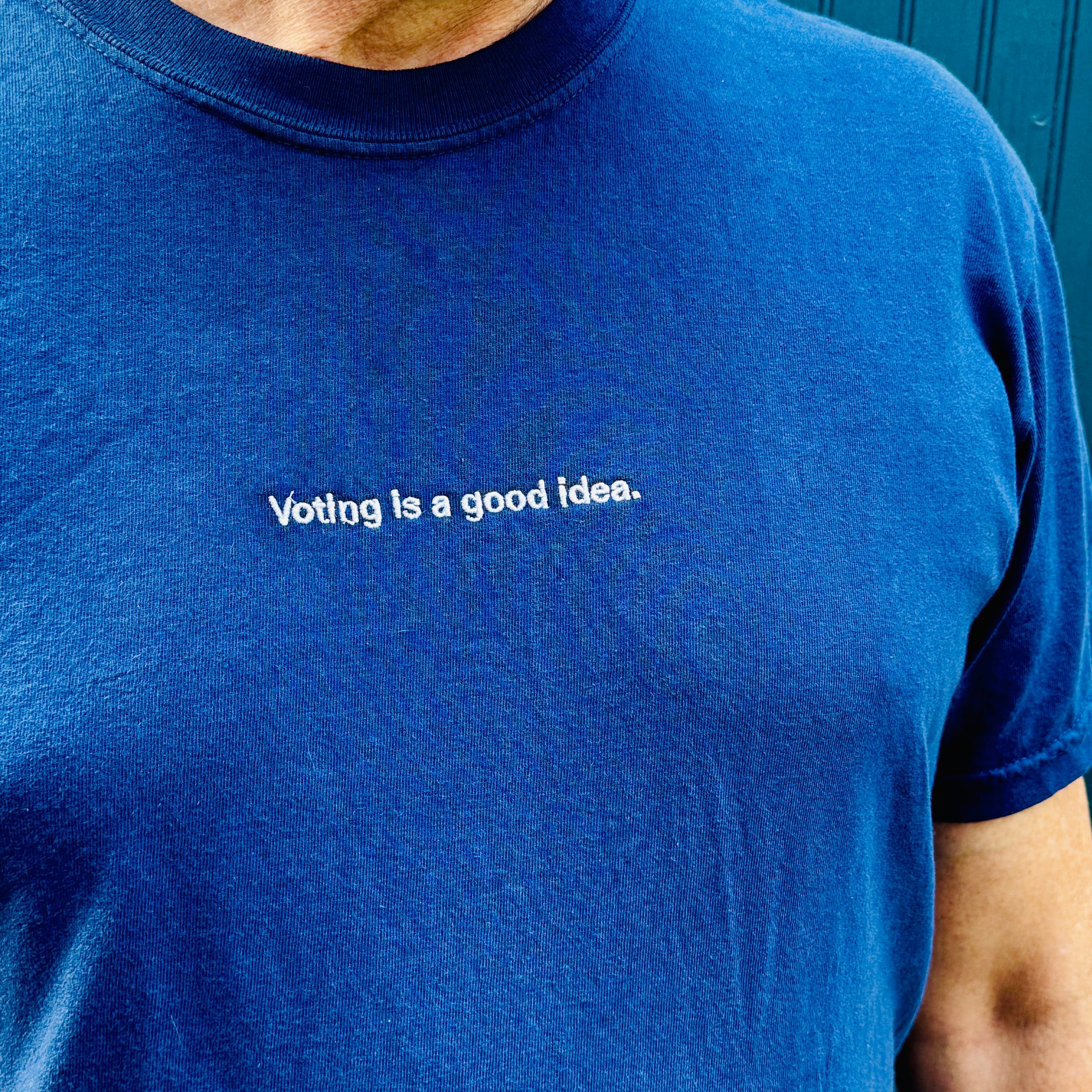 man wearing navy heavyweight unisex t-shirt with the phrase, voting is a good idea, embroidered in white on the front