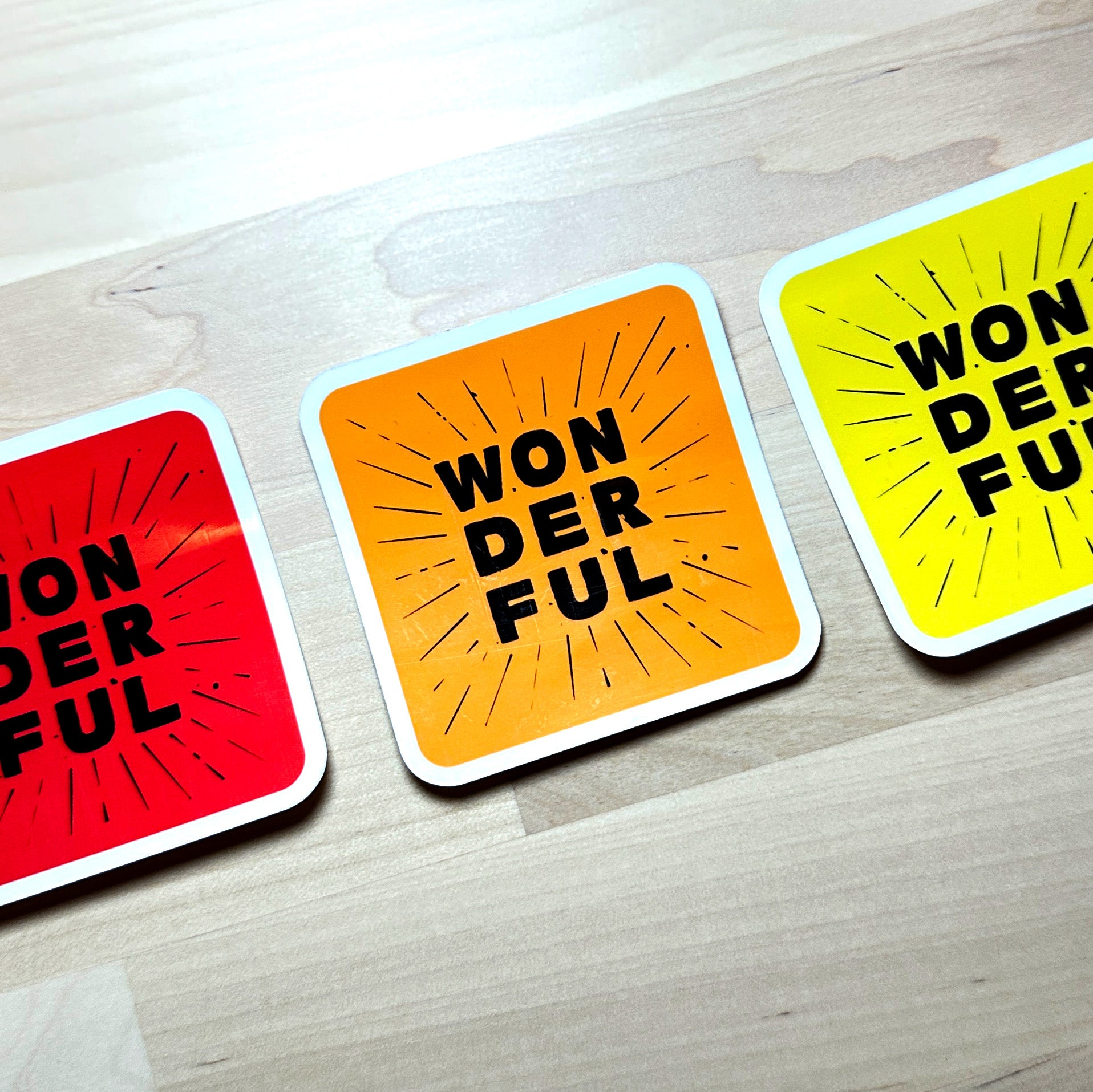 photo of 3 waterproof vinyl sticker with the word wonderful in 3 layers of black text on red, orange, and yellow background