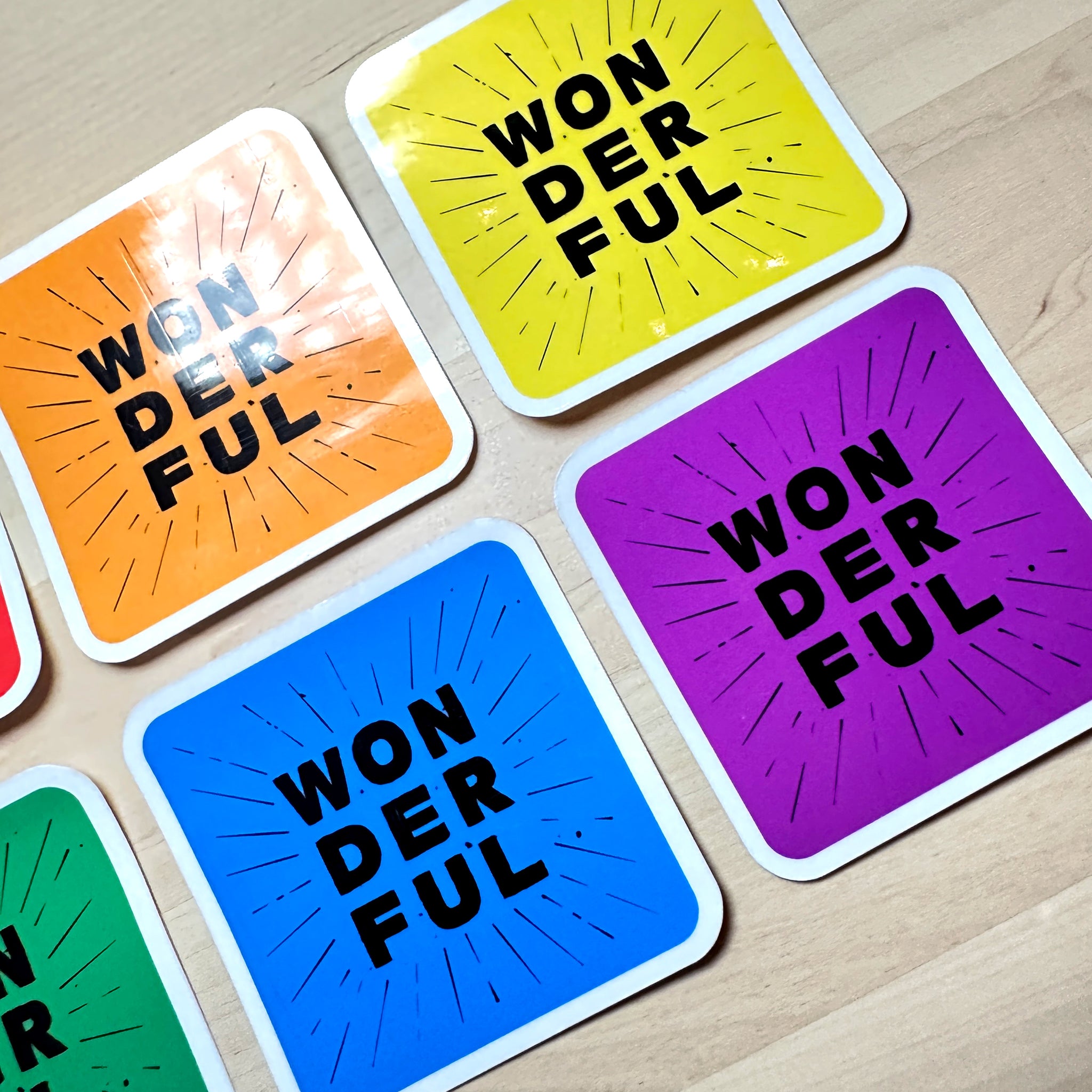 photo of 4 waterproof vinyl sticker with the word wonderful in 3 layers of black text on blue, orange, yellow and purple  background