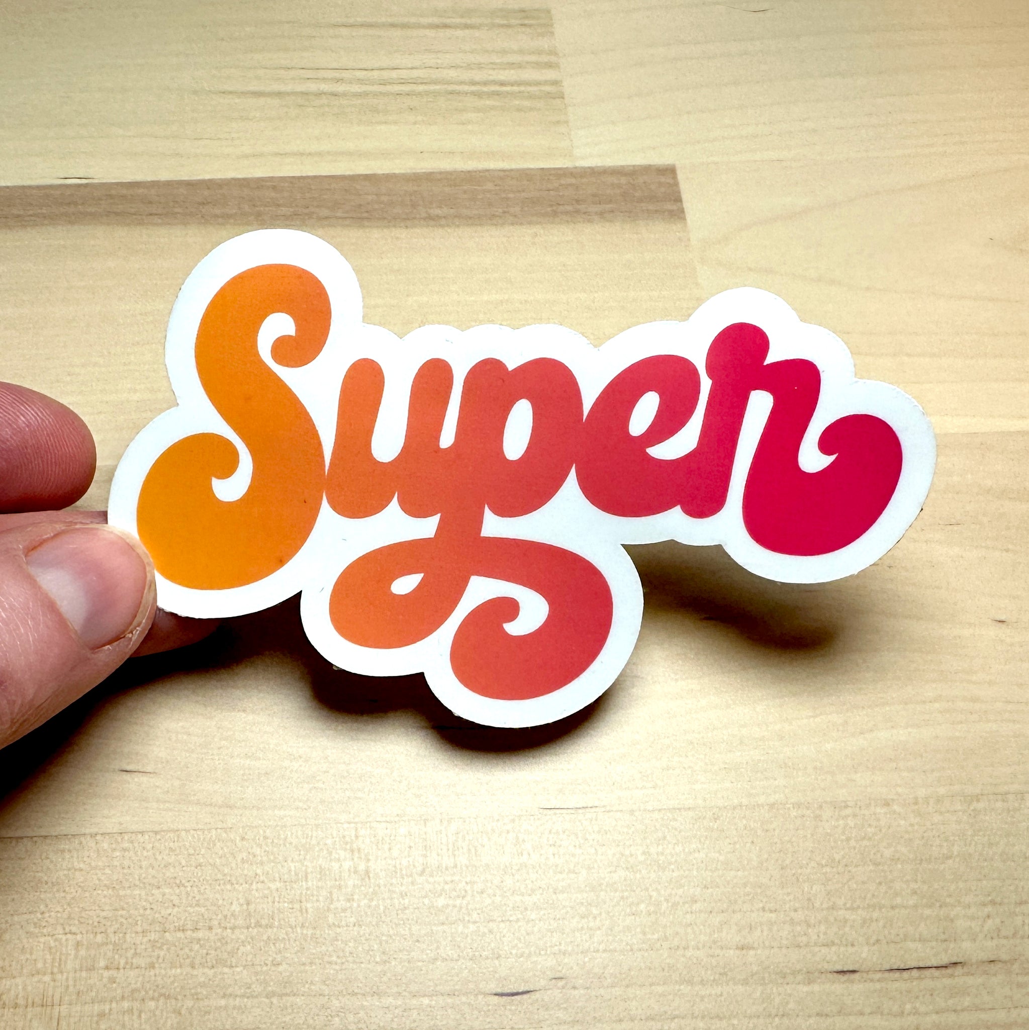 photo of a waterproof vinyl sticker with the word SUPER in an orange to red blend of color