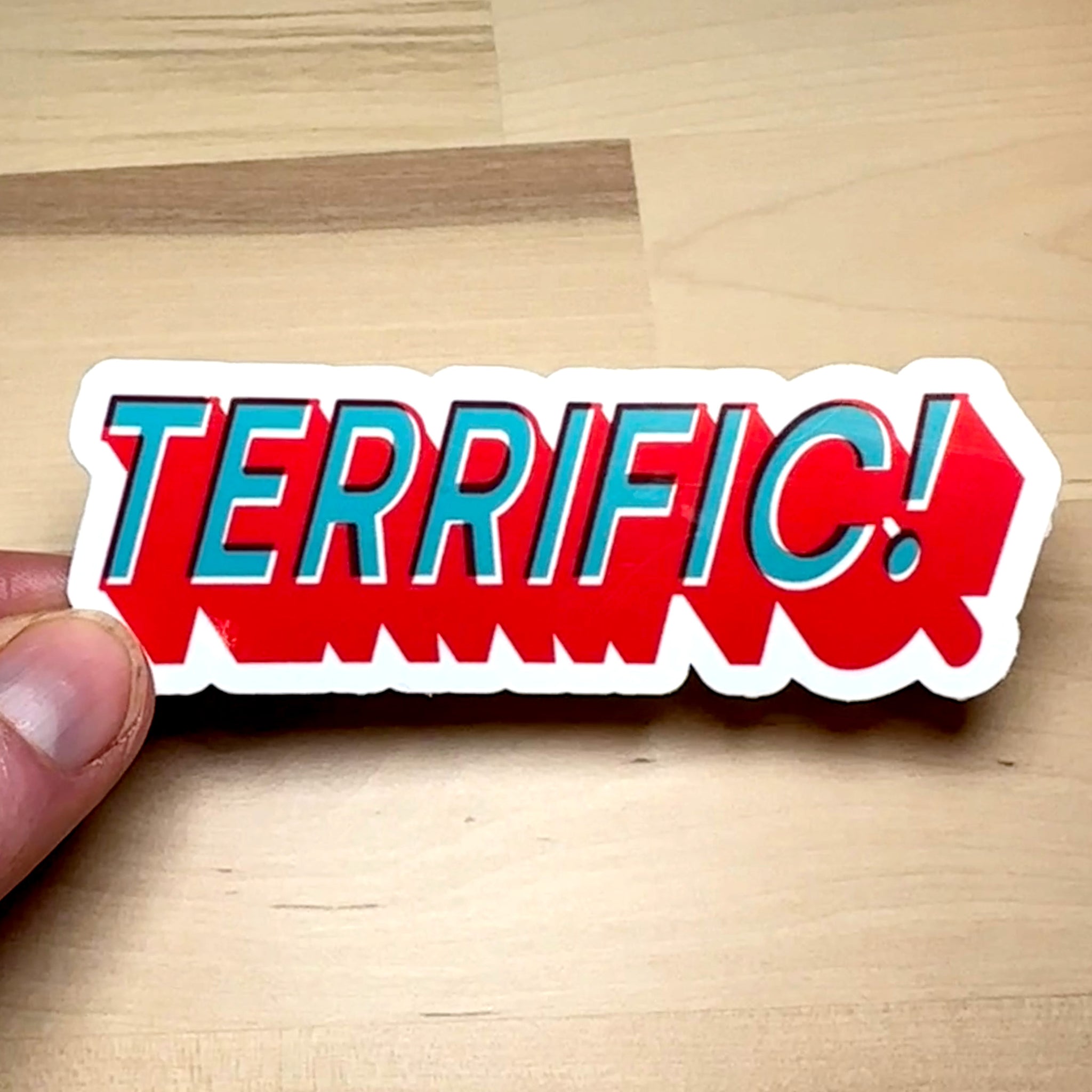 photograph of waterproof sticker of the word Terrific! in teal with a block red outline