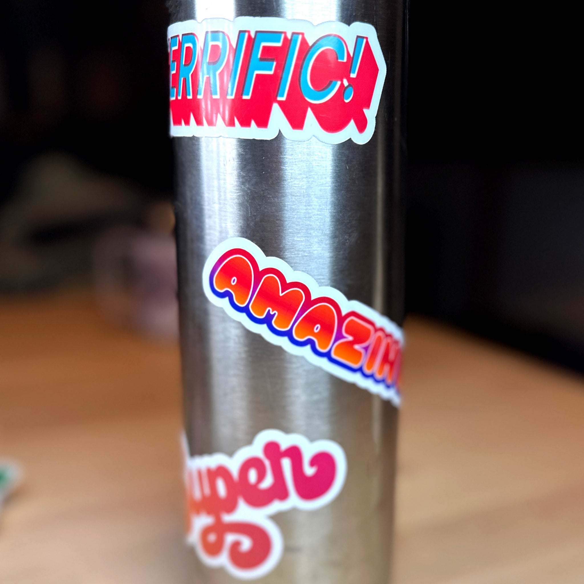 photograph of waterproof sticker of the word Terrific! in teal with a block red outline on a metal water bottle