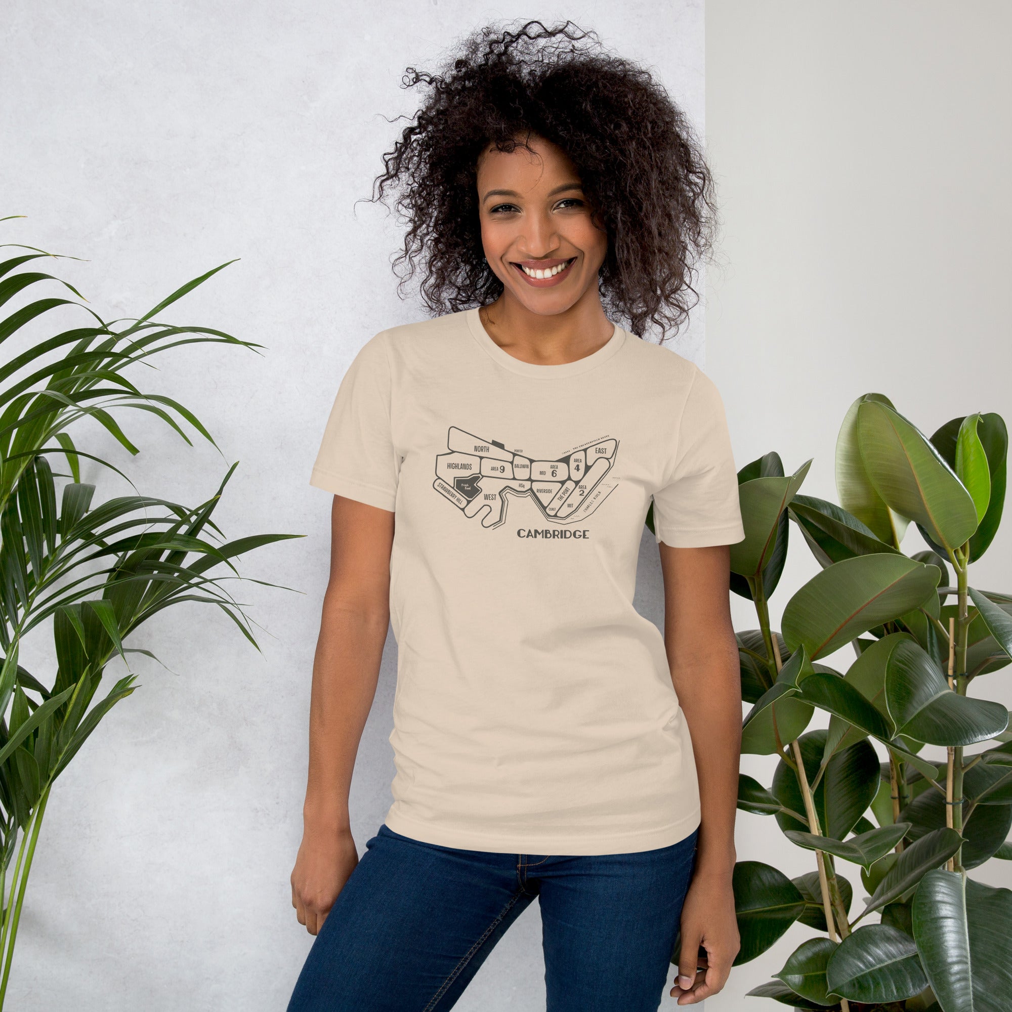 woman wearing cream, tan unisex t-shirt with a hand drawn map of cambridge, ma in dark grey