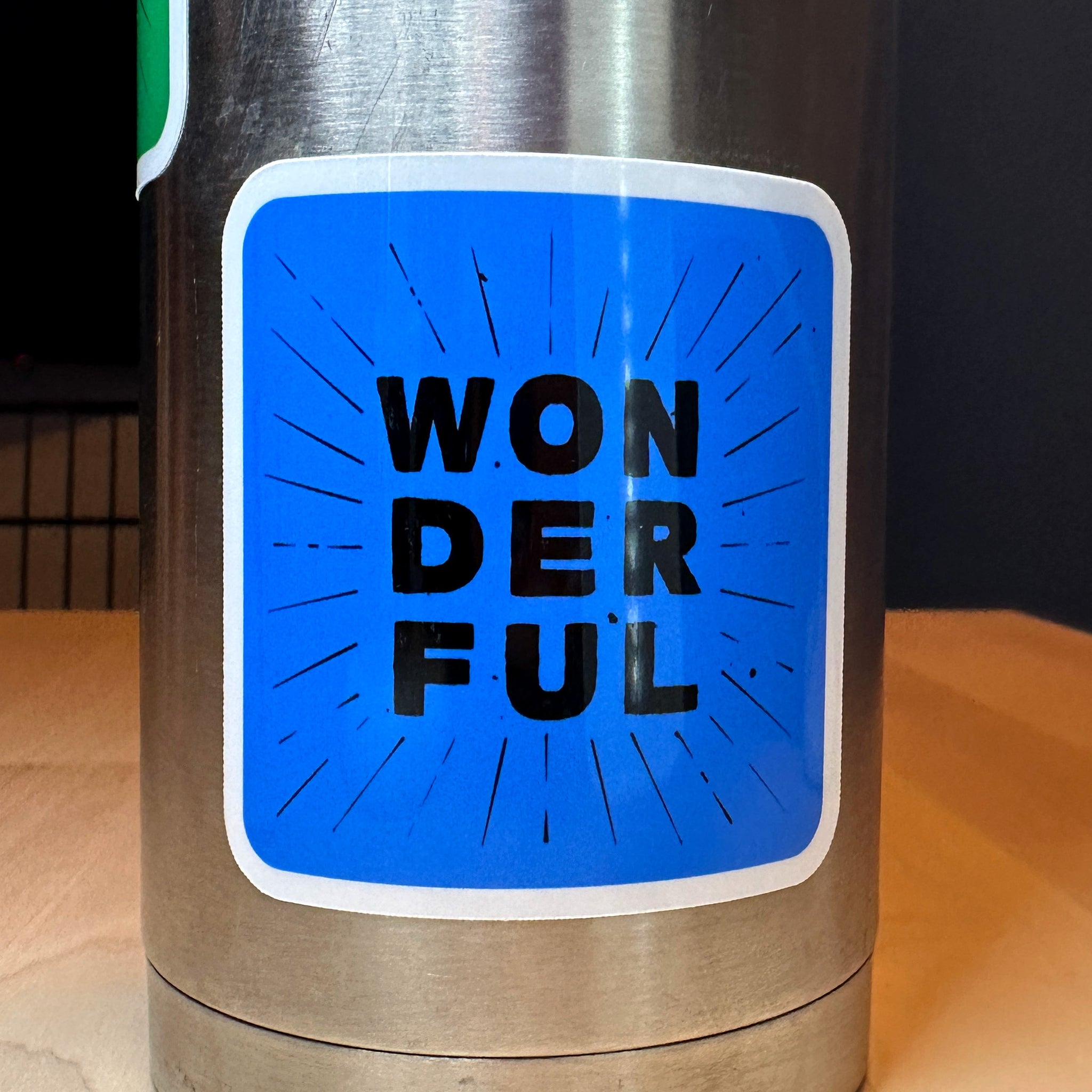 photo of waterproof vinyl sticker with the word wonderful in 3 layers of black text on blue background on a metal water bottle